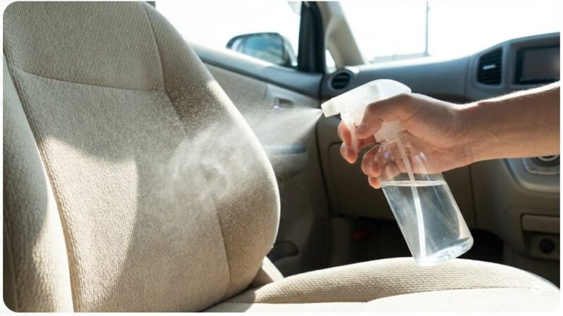 車のシートの汚れ部分に重曹水をスプレーボトルで吹きかけている様子
