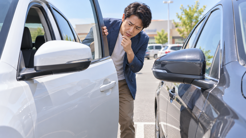 駐車場で自分の車のドアと隣の車との間隔を確認する男性