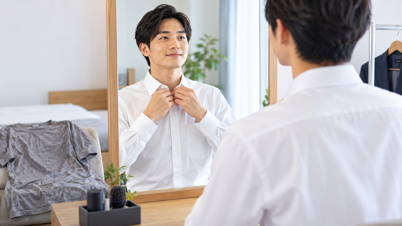 鏡の前で白い襟付きシャツを整えながら証明写真向けの服装を確認する男性